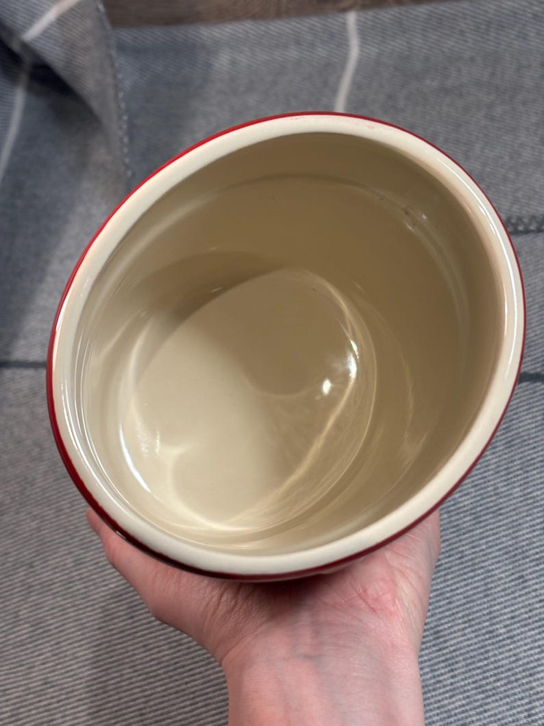 May include: A red ceramic container with a white interior. The container is empty and appears to be made of a durable material.