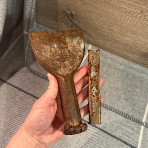 Puede incluir: Dos cinceles antiguos de metal oxidado. Uno tiene una hoja ancha y curvada y un mango. El otro es un cincel rectangular y estrecho. Ambas herramientas muestran signos de edad y desgaste, con un aspecto marrón y desgastado.