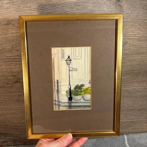 May include: A framed watercolour painting of a street scene with a lamppost and a street sign. The painting is in shades of grey and green, with a touch of white. The street sign reads "Park Lane".