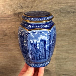 May include: Blue and white ceramic jar with a gold trim. The jar features a detailed illustration of York Minster, a famous cathedral in England. The jar is a decorative piece and has a lid.