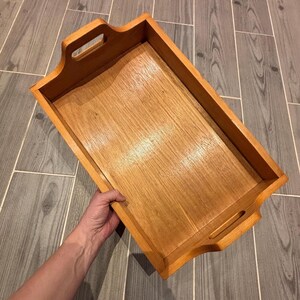 May include: A wooden serving tray with a natural wood finish and two handles. The tray is empty and ready to be filled with food or drinks.