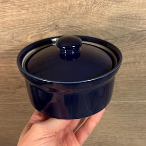 Può includere: Una zuccheriera in ceramica blu scuro con coperchio. La ciotola ha un bordo bianco e il coperchio ha un piccolo pomo.