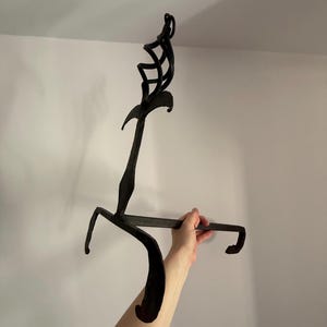 Peut inclure: Un outil de cheminée en fer forgé noir avec un dessus décoratif et une poignée incurvée. L'outil est tenu par la main d'une personne sur un fond blanc. L'outil a un crochet à l'extrémité.