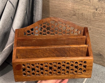 May include: A wooden desk organizer with a warm brown finish. The organizer features three compartments and decorative cut-out patterns. The top and bottom sections have intricate geometric designs, adding a touch of elegance to the functional piece.