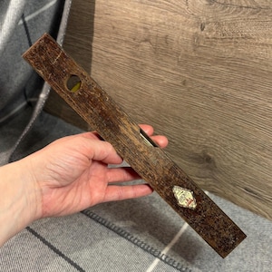 May include: A vintage wooden spirit level with a dark brown finish. The level has a bubble vial and a small label with text. The tool is held in a hand.