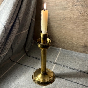 May include: A brass candlestick with a single white candle burning. The candlestick has a round base and a tall, slender stem.