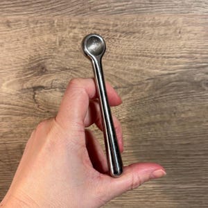 May include: A silver nutcracker with a rounded, smooth handle and a circular opening at the top.