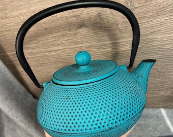 May include: A teal blue cast iron teapot with a black handle and a textured surface. The teapot has a round body and a small spout.