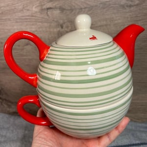 May include: A green and white striped ceramic teapot with a red lid and handle. The teapot has a matching cup with a red handle.