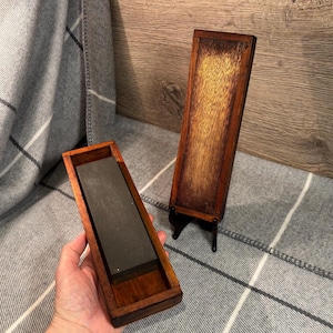 May include: Two wooden boxes with a dark brown finish. One box is open and contains a grey sharpening stone. The other box is closed and has a stand.