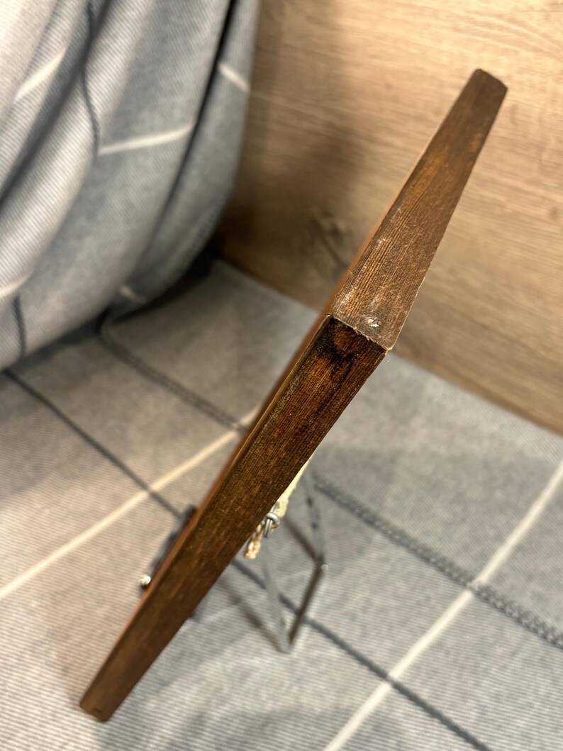 May include: A wooden picture frame with a dark brown finish. The frame is supported by a silver metal easel. The background is a gray and white plaid pattern.