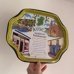 May include: A decorative metal tray featuring scenes from Avoca, Ireland, including buildings, a bridge, and the text "AVOCA location for Ballykissangel." The tray has a green and yellow border with Celtic knot designs.