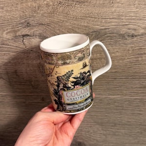 May include: White ceramic mug with a handle, featuring a vintage map design with the words "COCOA GUATIMALA" in a rectangular frame. The mug has a cream-coloured background and a detailed illustration.