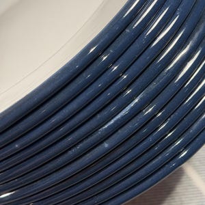 Pode incluir: Uma pilha de pratos redondos de cer&acirc;mica com um centro branco brilhante e uma borda larga azul-escura com uma s&eacute;rie de sulcos circulares conc&ecirc;ntricos em relevo que criam uma apar&ecirc;ncia texturizada e ranhurada na borda de cada prato.