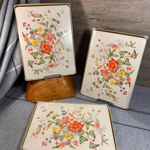 May include: Set of four floral table mats with a white background and colourful flowers. The mats are packaged in a clear plastic sleeve with a gold border and the text "CLOVER LEAF 4 Table Mats".