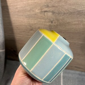 Op de afbeelding: Een kleine, keramische vaas met een geometrisch ontwerp. De vaas is blauw, groen en geel.