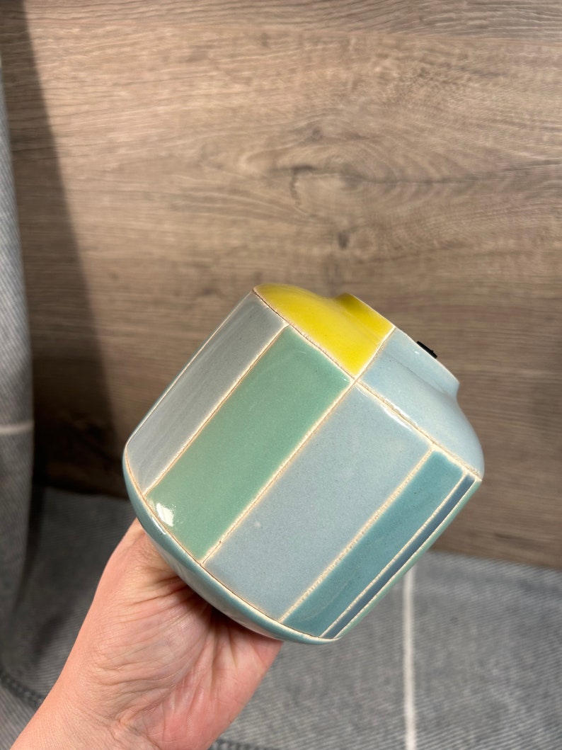 Op de afbeelding: Een kleine, keramische vaas met een geometrisch ontwerp. De vaas is blauw, groen en geel.