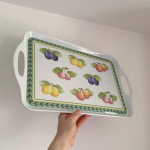Puede incluir: Bandeja rectangular blanca con asas, con un estampado de frutas. El diseño de la bandeja incluye ilustraciones de ciruelas, limones y cerezas. Un borde verde con un patrón de hojas enmarca el diseño de frutas.
