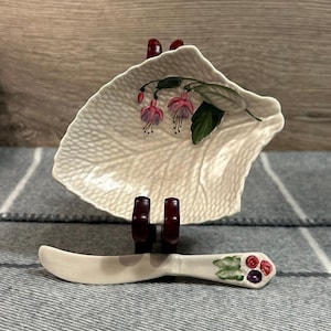 Könnte beinhalten: Eine weiße, blattförmige Schale aus Keramik mit einem bemalten Fuchsienblumenmuster. Ein passendes weißes Buttermesser aus Keramik mit einem bemalten Beerendesign ist enthalten.