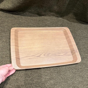 May include: A rectangular serving tray featuring a light brown wood grain pattern. The tray has a flat base with slightly raised, rounded edges and a smooth finish, displaying a consistent wood texture across the entire surface area.