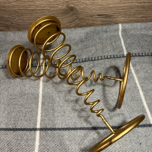 Peut inclure: Bougeoir en m&eacute;tal dor&eacute; avec un design en ressort. Le bougeoir a trois bases circulaires et un design en spirale.