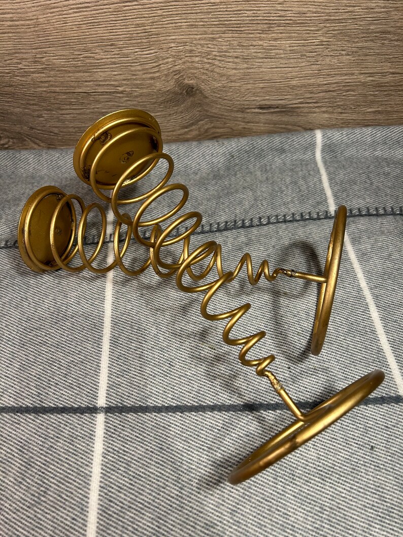 Peut inclure: Bougeoir en m&eacute;tal dor&eacute; avec un design en ressort. Le bougeoir a trois bases circulaires et un design en spirale.