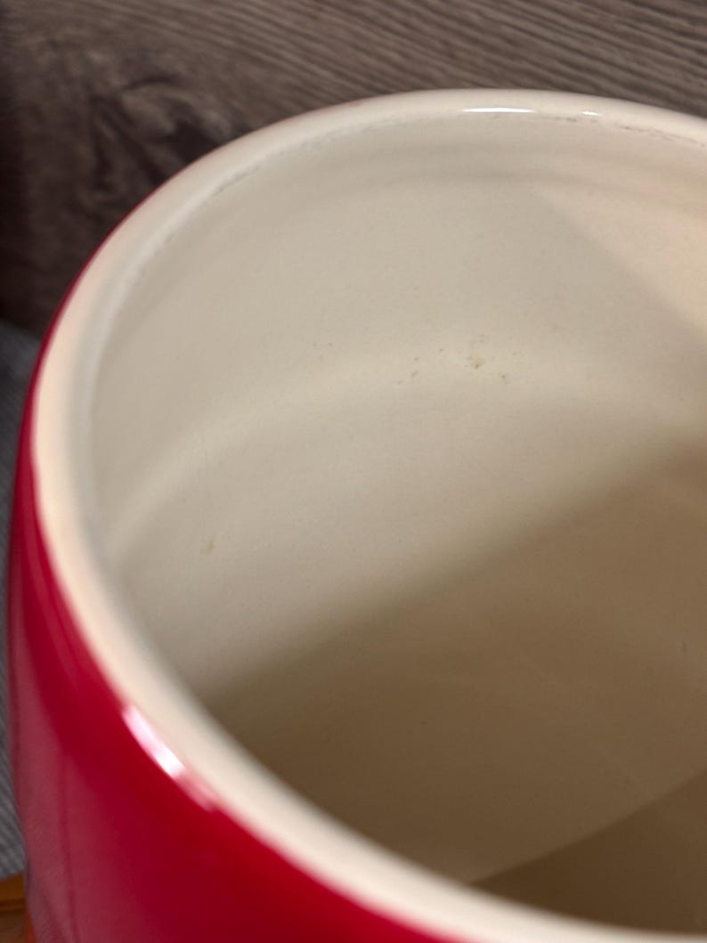 May include: A red ceramic canister with a white interior. The canister is empty and has a smooth, glossy finish.