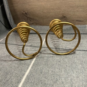 Peut inclure: Deux bougeoirs en m&eacute;tal dor&eacute; avec un design en spirale. Les bougeoirs sont sur une surface ray&eacute;e gris et blanc.
