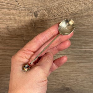 May include: Silver spoon with a colorful, patterned handle. The spoon has the words "GOODLAND HOTEL, VIRGINIA" engraved on the back.