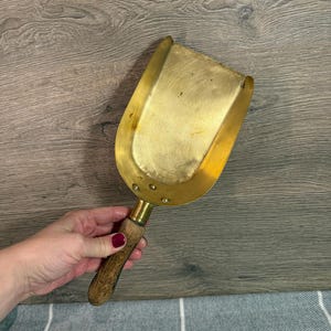 Peut inclure: Une pelle en laiton vintage avec un manche en bois. La pelle a une forme rectangulaire avec des bords arrondis et est fixée à un manche en bois. Le manche est en bois brun clair. La pelle est de couleur or brillant.