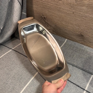 May include: A silver serving dish with wooden handles. The dish is oval shaped and has a smooth, shiny surface.