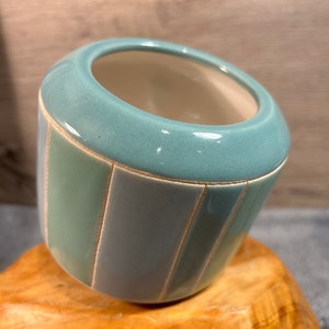 Op de afbeelding: Een lichtblauwe keramische plantenpot met verticale strepen in een lichtere tint blauw en wit. De pot heeft een afgeronde vorm en een gladde, geglazuurde afwerking.