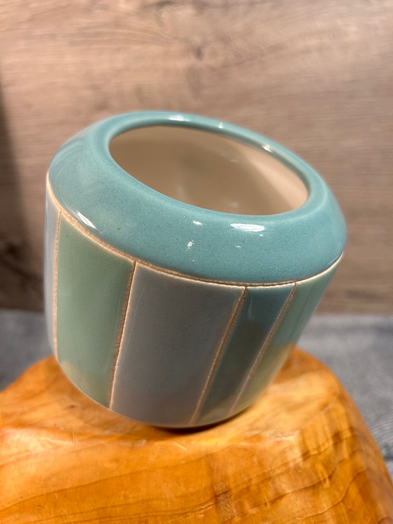 Op de afbeelding: Een lichtblauwe keramische plantenpot met verticale strepen in een lichtere tint blauw en wit. De pot heeft een afgeronde vorm en een gladde, geglazuurde afwerking.