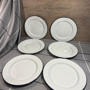 Pode incluir: Um conjunto de seis pratos redondos de esmalte branco, cada um com uma superf&iacute;cie lisa e uma borda fina azul-escura. Os pratos est&atilde;o dispostos em duas filas de tr&ecirc;s, exibindo um design limpo e uniforme com um acabamento brilhante.