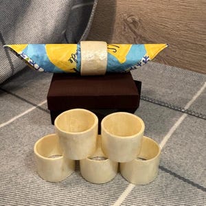 Könnte beinhalten: Satz mit sechs weißen Serviettenringen aus natürlichen Materialien. Die Ringe sind übereinander gestapelt.