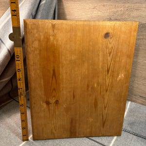 May include: A rectangular wooden cutting board with a natural wood grain finish. The board is approximately 14 inches tall. A folding ruler is positioned next to the board, showing measurements in inches. The wood has visible knots and a warm, light brown color.