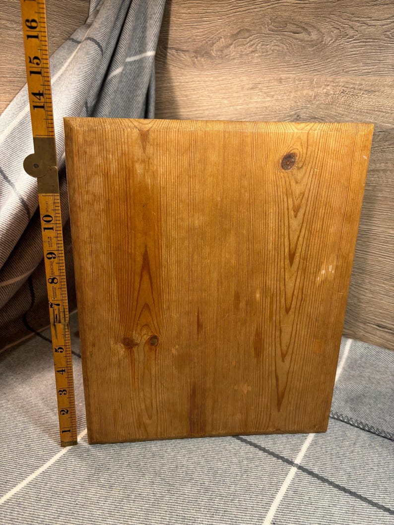 May include: A rectangular wooden cutting board with a natural wood grain finish. The board is approximately 14 inches tall. A folding ruler is positioned next to the board, showing measurements in inches. The wood has visible knots and a warm, light brown color.