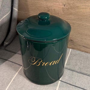 May include: A set of three ceramic mugs with a speckled, cream-coloured glaze. Each mug features a different hand-painted floral design in shades of blue, green, and yellow. The mugs have a simple, modern shape.