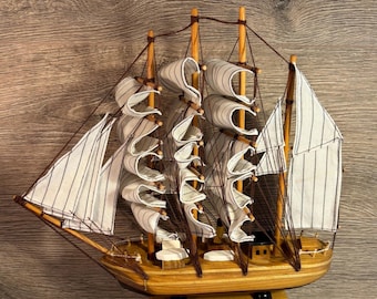 May include: A wooden model sailboat with white and brown striped sails and rigging. The ship has a light brown hull and is mounted on a wooden base. The sails are billowing, suggesting the ship is at sea. A decorative nautical item.