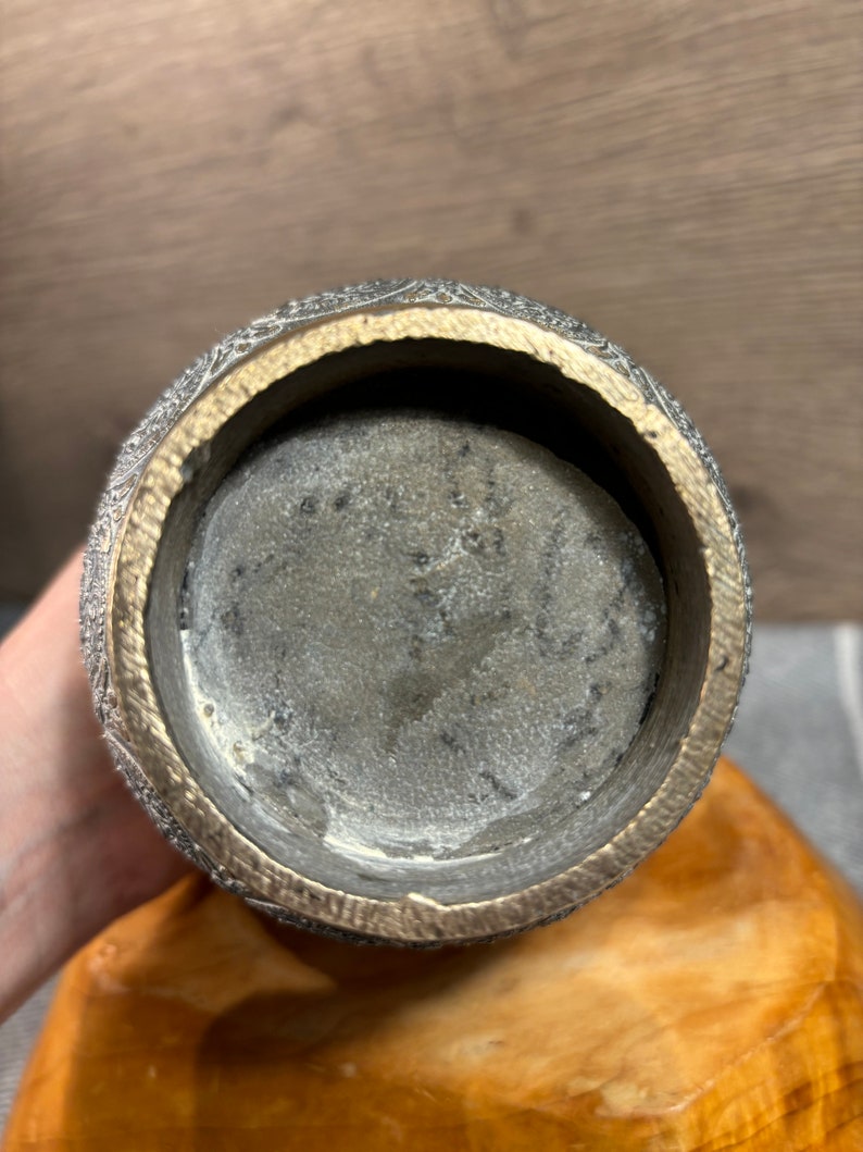 K&ouml;nnte beinhalten: Der Boden einer dekorativen Vase aus Silber und Gold mit einem komplizierten Design. Das Innere der Vase ist sichtbar und scheint aus einem dunkleren Metall zu sein.