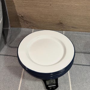 Pode incluir: Uma pilha de pratos redondos com interior branco e borda azul escura. Os pratos repousam sobre uma balan&ccedil;a de cozinha digital preta que exibe um peso de 362,1 gramas, fornecendo uma medi&ccedil;&atilde;o clara do peso total da pilha nesta vista.