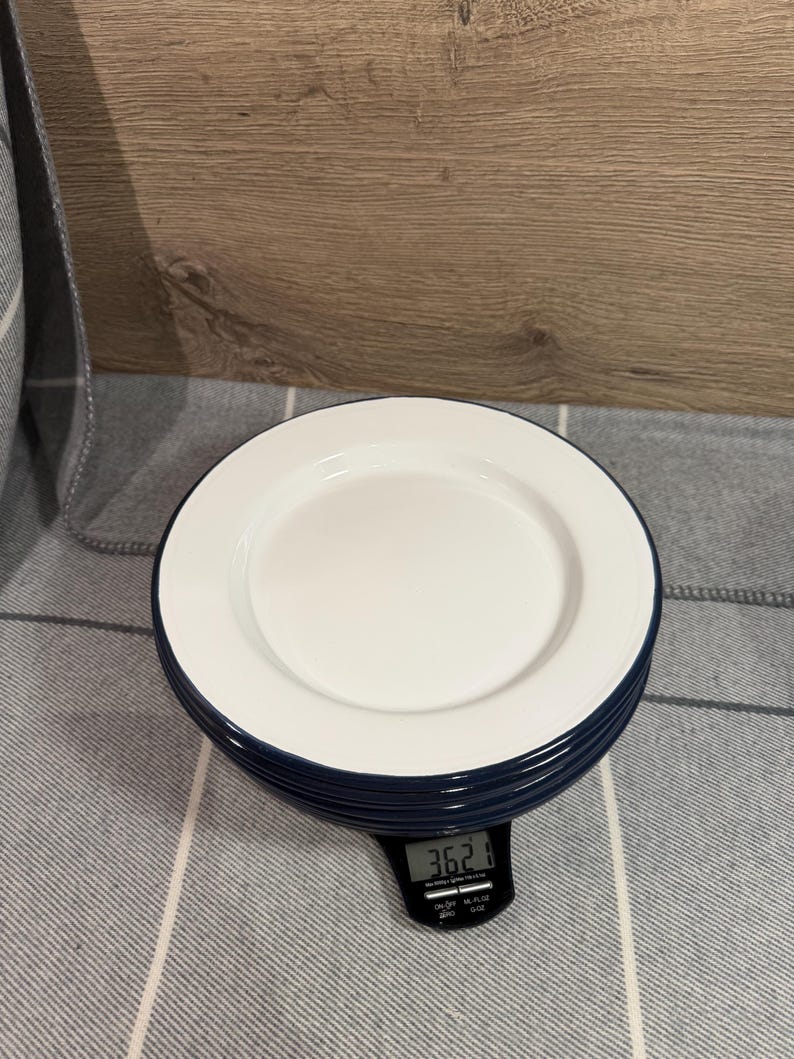Pode incluir: Uma pilha de pratos redondos com interior branco e borda azul escura. Os pratos repousam sobre uma balan&ccedil;a de cozinha digital preta que exibe um peso de 362,1 gramas, fornecendo uma medi&ccedil;&atilde;o clara do peso total da pilha nesta vista.