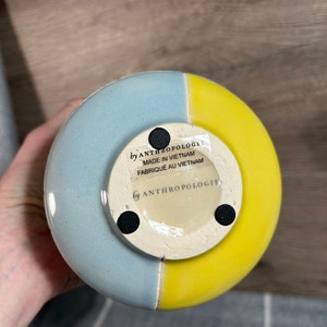 Op de afbeelding: Een blauwe en gele keramische vaas met een ronde basis. De vaas heeft een label op de bodem met de tekst "by Anthropologie Made in Vietnam Fabrique au Vietnam".