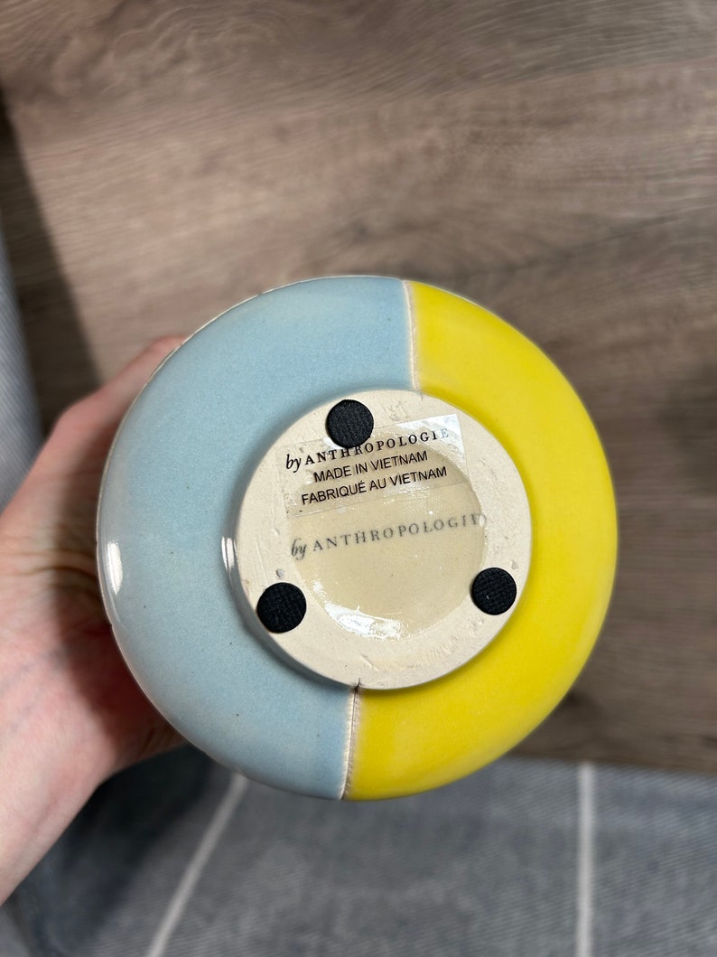 Op de afbeelding: Een blauwe en gele keramische vaas met een ronde basis. De vaas heeft een label op de bodem met de tekst "by Anthropologie Made in Vietnam Fabrique au Vietnam".