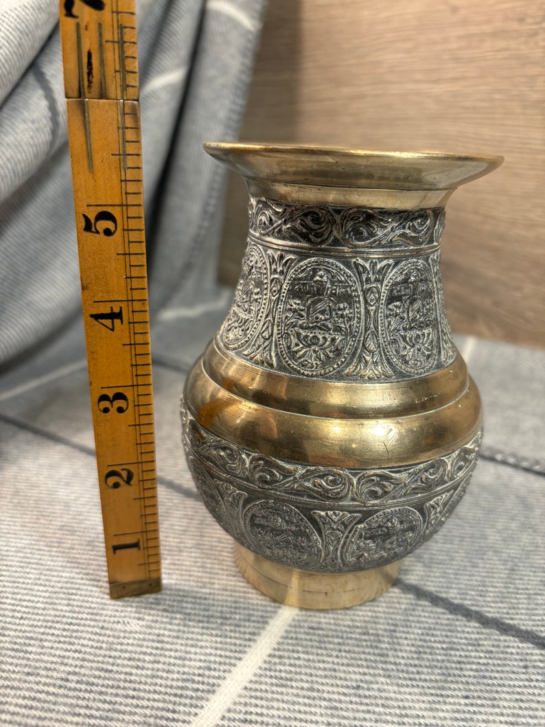 K&ouml;nnte beinhalten: Eine kleine, verzierte Messingvase mit einem komplizierten gravierten Design. Die Vase ist etwa 13 cm hoch und hat eine goldfarbene Oberfl&auml;che.