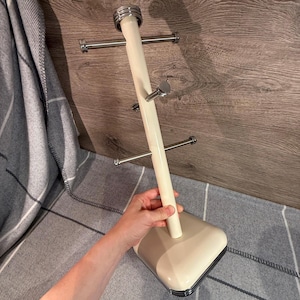 May include: Cream-colored mug tree with a square base and a vertical pole with multiple horizontal arms. The arms are made of silver metal. The top of the pole has a silver metal band. The mug tree is designed to hold multiple mugs.
