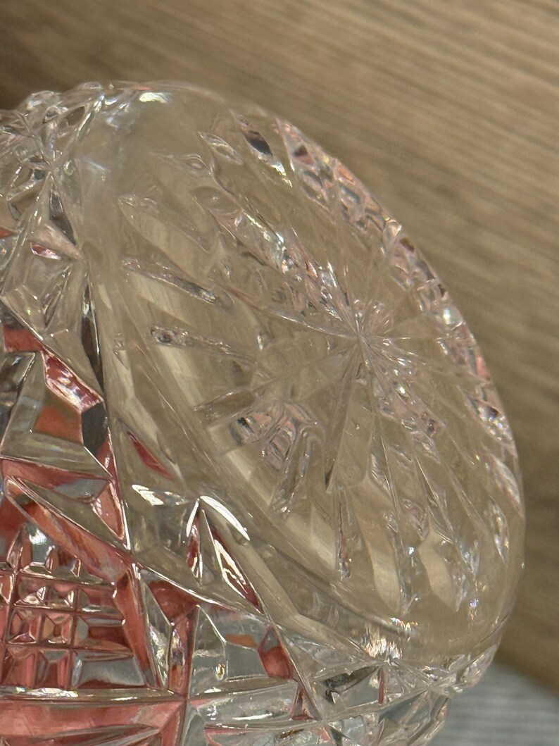 Op de afbeelding: Close-up van een heldere, geslepen glazen kom. De kom heeft een geometrisch patroon met diamant- en sterrenmotieven. Het licht reflecteert op de facetten, waardoor een sprankelend effect ontstaat. De kom is waarschijnlijk bedoeld om te serveren of tentoon te stellen.