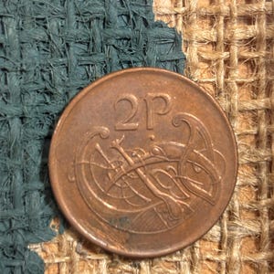 Puede incluir: Una moneda de 2 peniques del Reino Unido. La moneda es de cobre y presenta un dise&ntilde;o de nudo celta.