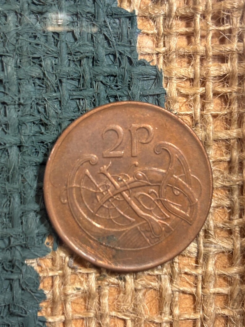 Puede incluir: Una moneda de 2 peniques del Reino Unido. La moneda es de cobre y presenta un dise&ntilde;o de nudo celta.