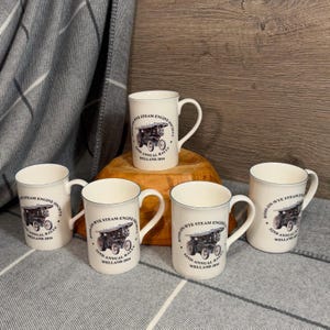 May include: Five white ceramic mugs with black and blue designs. Each mug features a steam engine illustration and the text "Ross-on-Wye Steam Engine Society 2nd Annual Rally Welland 2016".